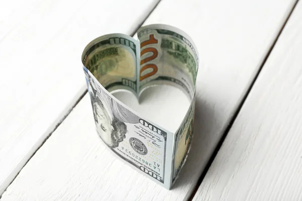 Dollars folded into heart on wooden background — Stock Photo, Image
