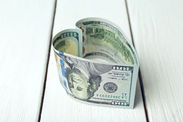 Dollars folded into heart on wooden background — Stock Photo, Image