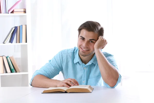 Jovem homem lendo livro à mesa no quarto — Fotografia de Stock