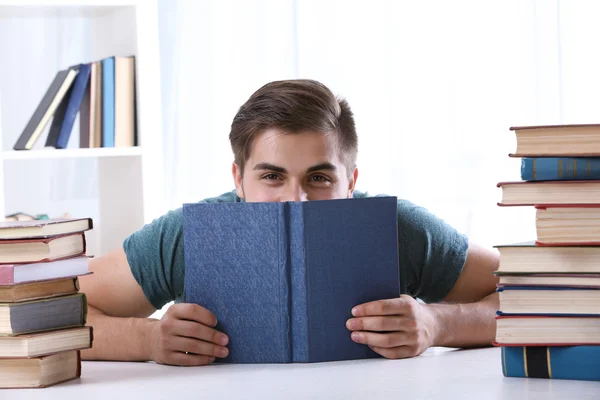 Junger Mann liest Buch am Tisch im Zimmer — Stockfoto