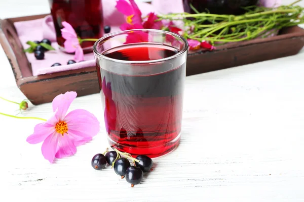 Glass of fresh blackcurrant juice on wooden table near tray with flowers, closeup — Stock Photo, Image