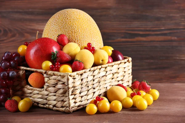 Ассортимент свежих фруктов в плетеной корзине на деревянном фоне — стоковое фото