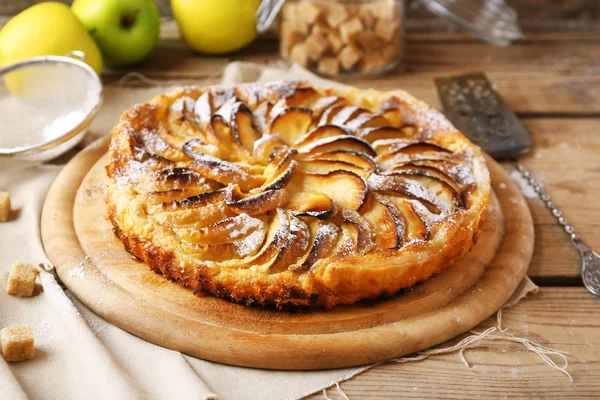 Домашній яблучний пиріг на обробній дошці та свіжі яблука на дерев'яному фоні — стокове фото