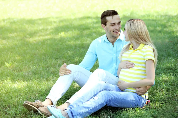 Junge schwangere Frau mit Ehemann sitzt auf grünem Gras im Park — Stockfoto