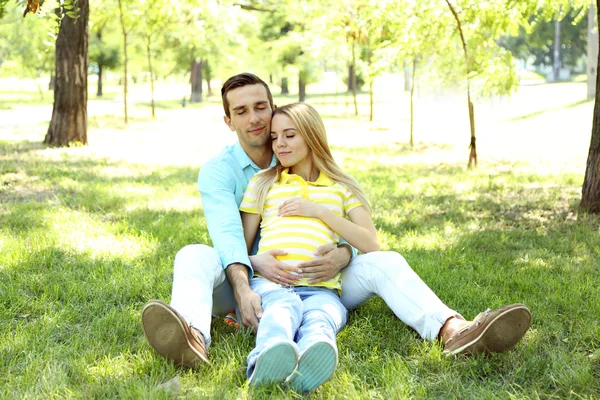 Jonge zwangere vrouw met man zittend op groen gras in park — Stockfoto