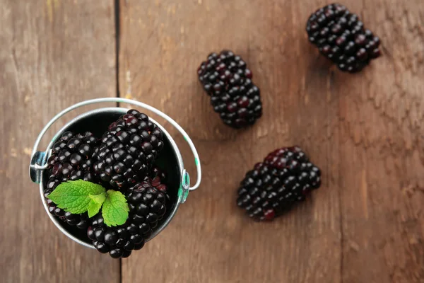 Ripe blackberries with green leaves in small metal bucket on wooden table, top view — Stock Photo, Image