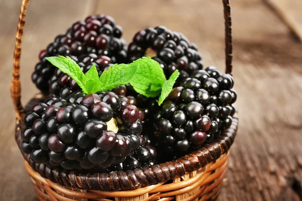 熟透的黑莓，绿色的叶子在柳条篮子里的木桌前，特写 — 图库照片