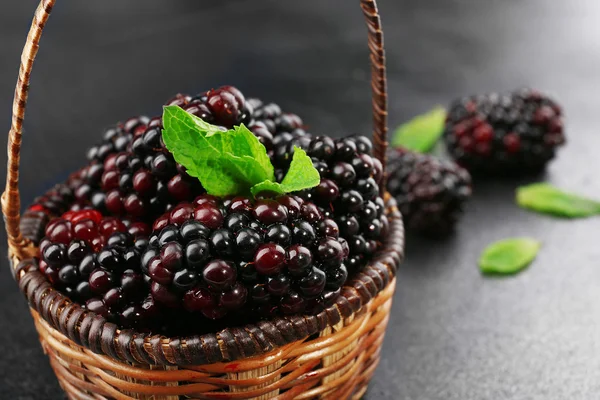 Ripe blackberries with green leaves in wicker basket on dark surface, closeup — Stock Photo, Image