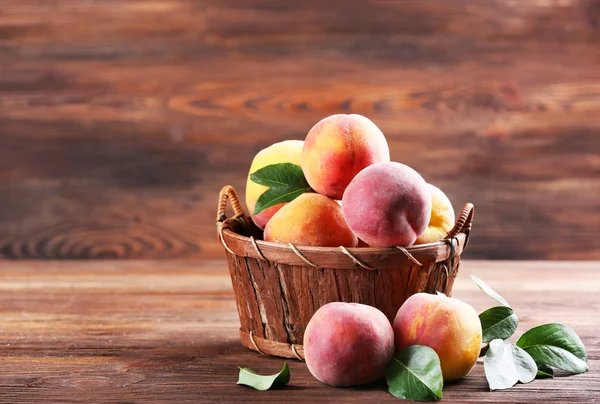 Fresh peaches in wicker basket on wooden background — Stock Photo, Image