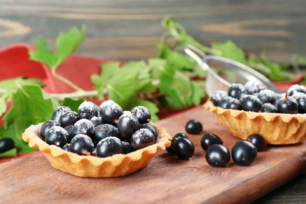 Délicieuses tartes croustillantes aux cassis sur planche à découper en bois, gros plan — Photo