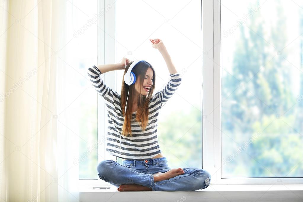 Woman listening music in headphones on windowsill background