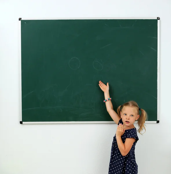 Liten flicka pekar på något på svarta tavlan — Stockfoto