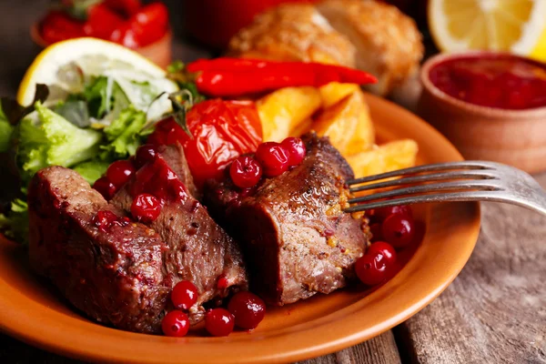 Вкусное жареное мясо с клюквенным соусом, салат и жареные овощи на тарелке, на деревянном фоне — стоковое фото