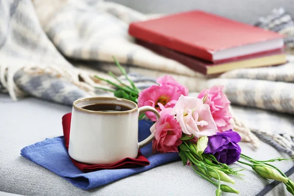 Cup of coffee with flowers near books on sofa in room — Stock Photo, Image