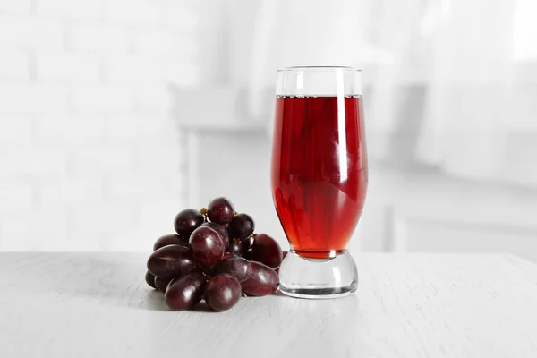 Glas sap en rijpe druiven in kom op houten tafel — Stockfoto