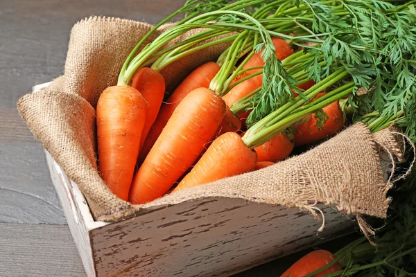 Fresh organic carrots in box with sackcloth on wooden table, closeup — Stock Photo, Image