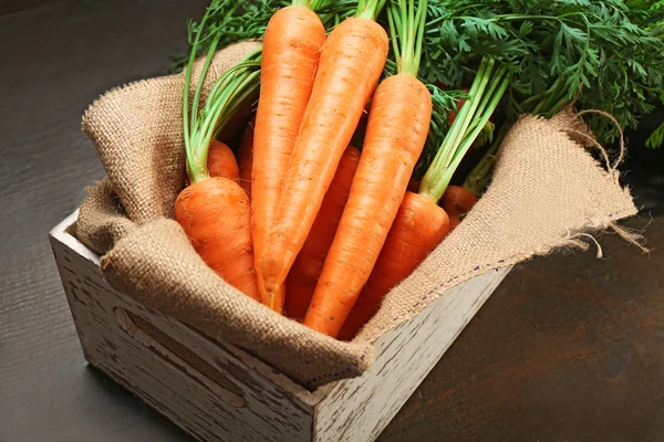 Zanahorias orgánicas frescas en caja con saco sobre mesa de madera, primer plano — Foto de Stock