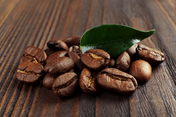 Koffie bonen met blad op houten achtergrond — Stockfoto