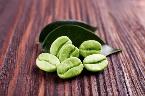 Groene koffiebonen met bladeren op houten achtergrond — Stockfoto