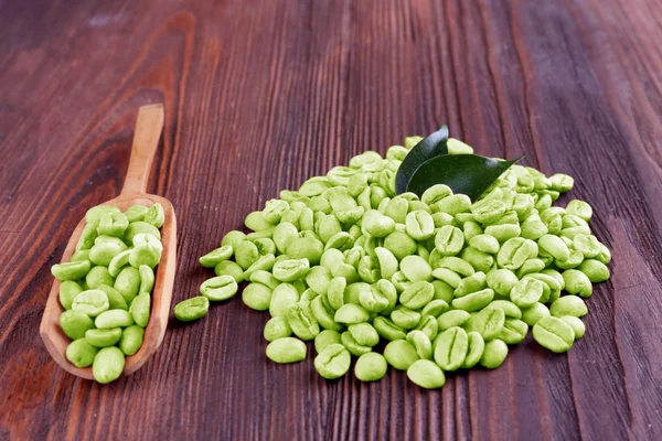 Grains de café verts avec feuilles et cuillère sur table en bois fermer — Photo