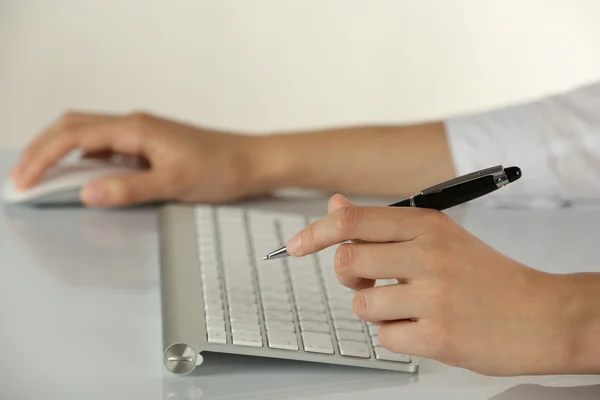 Mãos femininas segurando caneta e mouse de computador no fundo claro — Fotografia de Stock