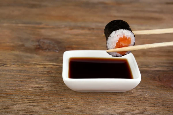 Dipping roll in sauce on wooden table — Stock Photo, Image