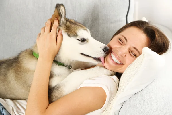 Mujer con su perro malamute en el sofá —  Fotos de Stock