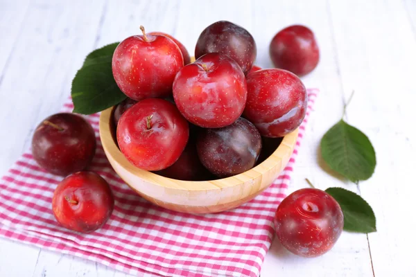 Ripe plums in bowl on wooden table with napkin, closeup — Stock Photo, Image