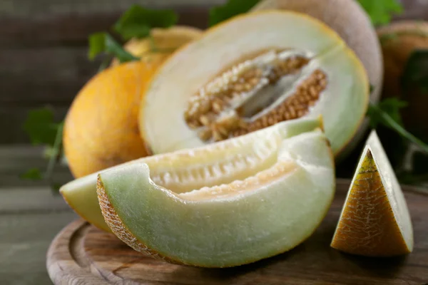 Rijpe meloenen met groene bladeren op houten tafel close-up — Stockfoto