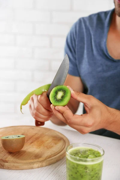 Ung man peeling kiwi, förbereda apelsinjuice — Stockfoto