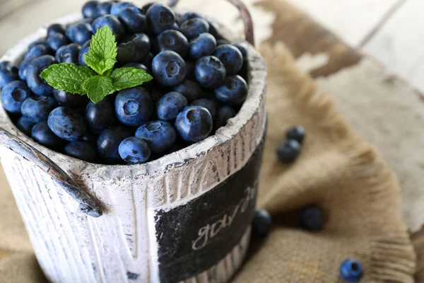 Tasty ripe blueberries with green leaves in bucket on table close up — Stock Photo, Image