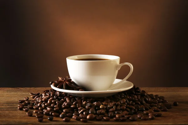 Tasse de café avec des grains sur table en bois sur fond sombre — Photo