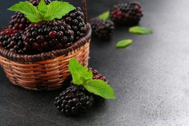 Karanlık yüzeyi, closeup hasır sepet içinde yeşil yaprakları ile olgun böğürtlen