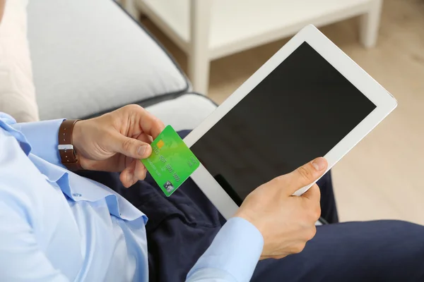 Man holding credit card and tablet on sofa in room — Stock Photo, Image