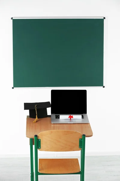 Scrivania con computer portatile, cappello master e diploma in aula — Foto Stock