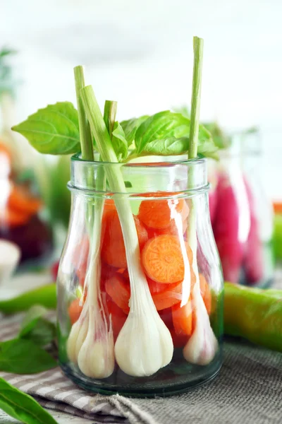 Frisches Gemüse in Glasflaschen auf dem Tisch vor leicht verschwommenem Hintergrund — Stockfoto