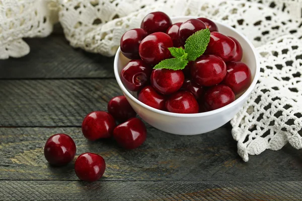 Cerezas dulces con hojas verdes en cuenco, sobre fondo de madera —  Fotos de Stock