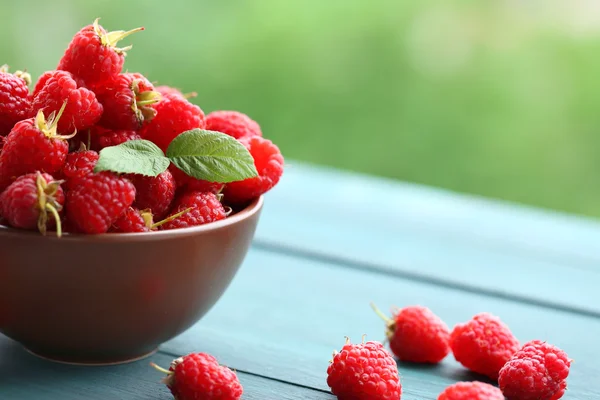 Fresh raspberries in bowl on wooden table on blurred nature background — Stock Photo, Image