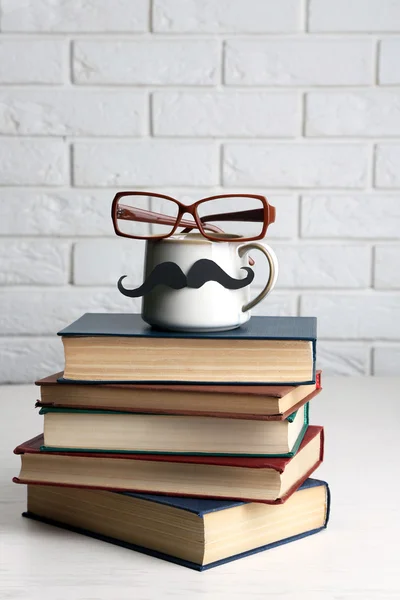 Vintage boeken en cup met snor op houten tafel op bakstenen muur achtergrond — Stockfoto