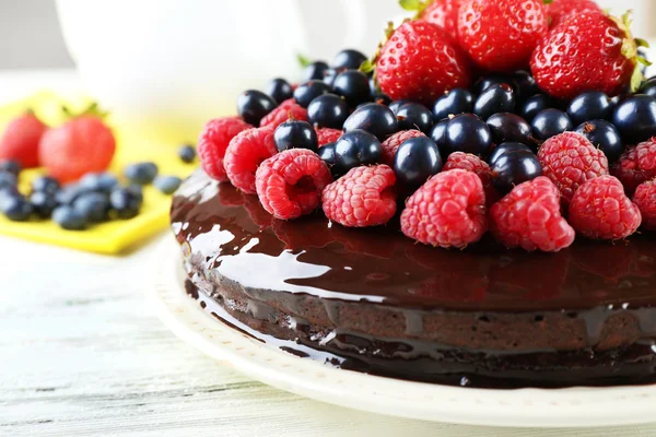 Delicioso pastel de chocolate con bayas de verano en la mesa de madera blanca, primer plano — Foto de Stock