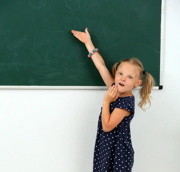 Liten flicka pekar på något på svarta tavlan — Stockfoto