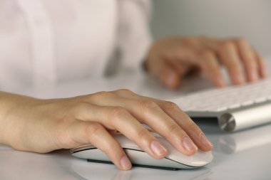 Klavyede yazan ve arka planda bilgisayar faresi tutan kadın eller