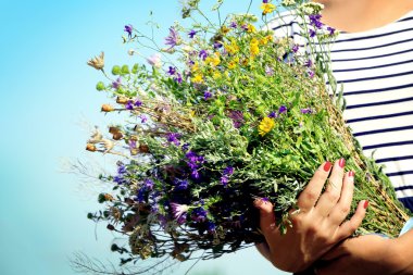 Mavi gökyüzü arka plan üzerinde çiçekler buket eller