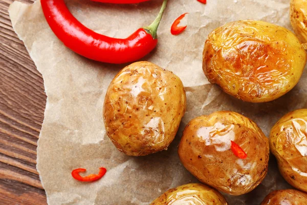 Baked spicy potatoes on parchment on wooden table, closeup — Stock Photo, Image