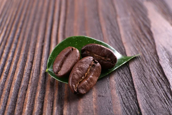 Chicchi di caffè con foglia su sfondo di legno — Foto Stock