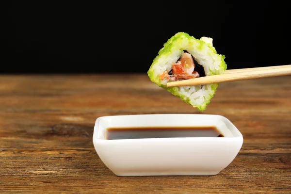 Dipping roll in sauce on dark background — Stock Photo, Image