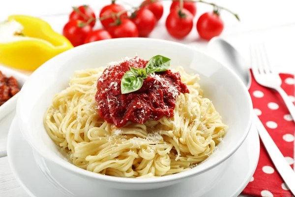 Спагетти с томатным соусом и сыром на белой тарелке, на цветном деревянном фоне — стоковое фото