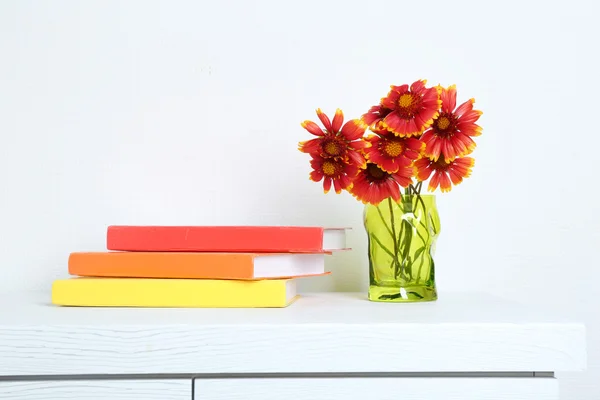 Mooie bloemen in vaas met boeken over muur achtergrond — Stockfoto