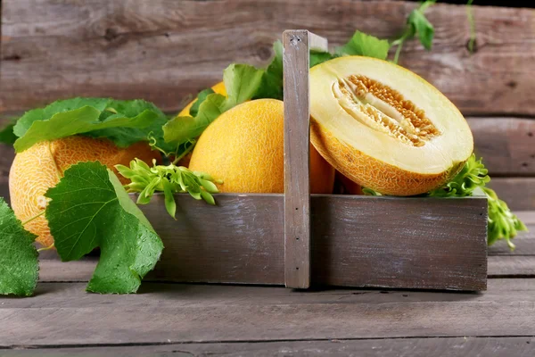 Ripe melons with green leaves in crate on table close up — Stock Photo, Image