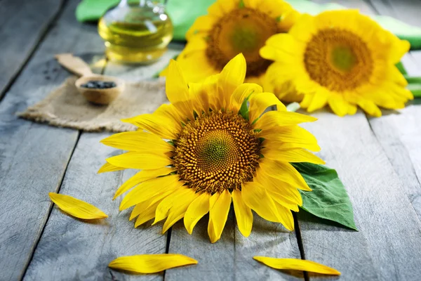 Beautiful bright sunflowers with bottle of oil on wooden table close up — Stock Photo, Image